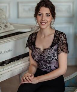 A woman in a black shirt sitting next to a piano.